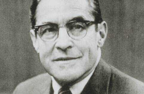 Headshot of an older man in a suit and glasses.