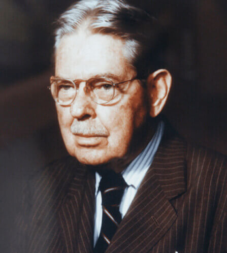 Color photo of an older man in a suit and tie, wearing glasses.